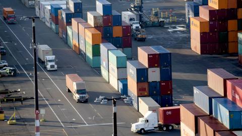 A large truck drives down a road lined with shipping containers.